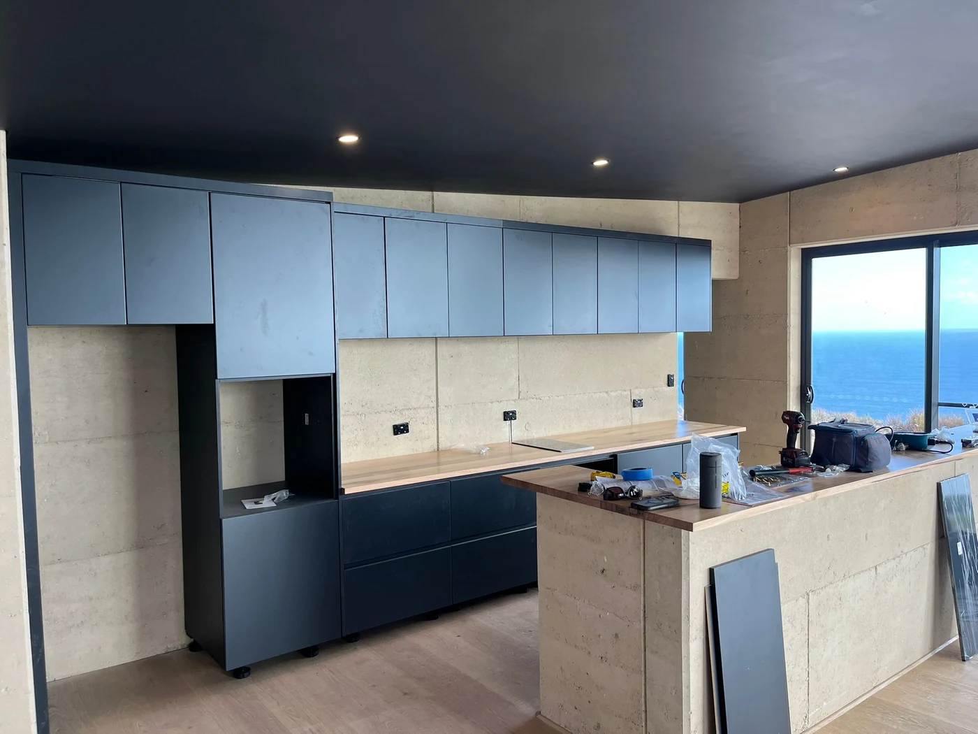 George Group-supplied dark kitchen cabinetry being installed in an overseas coastal residence