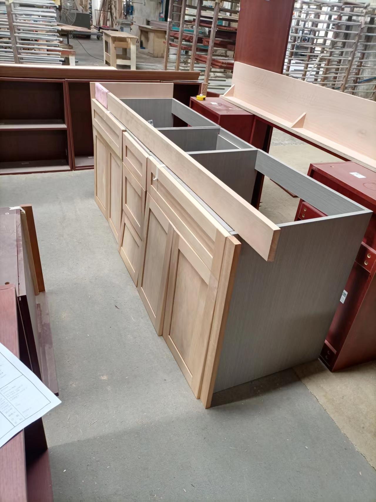 Angled view of assembled light wood base cabinet units in a woodworking factory