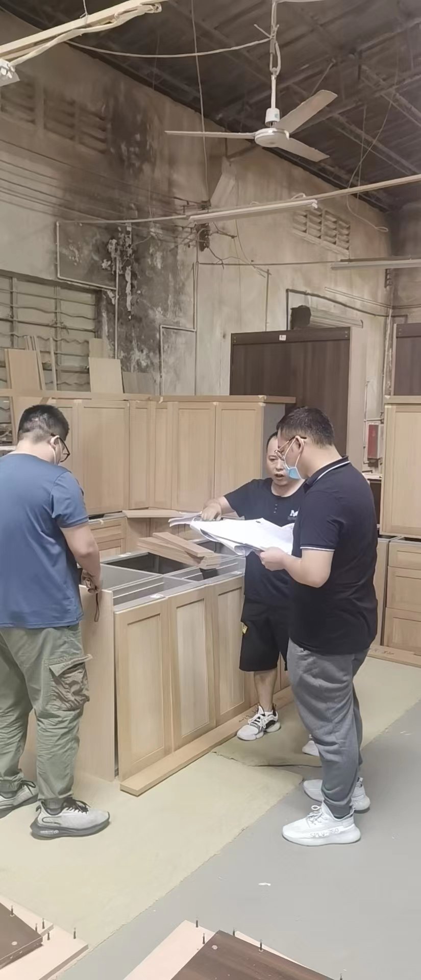 Workshop team consulting printed plans beside unfinished wooden cabinets