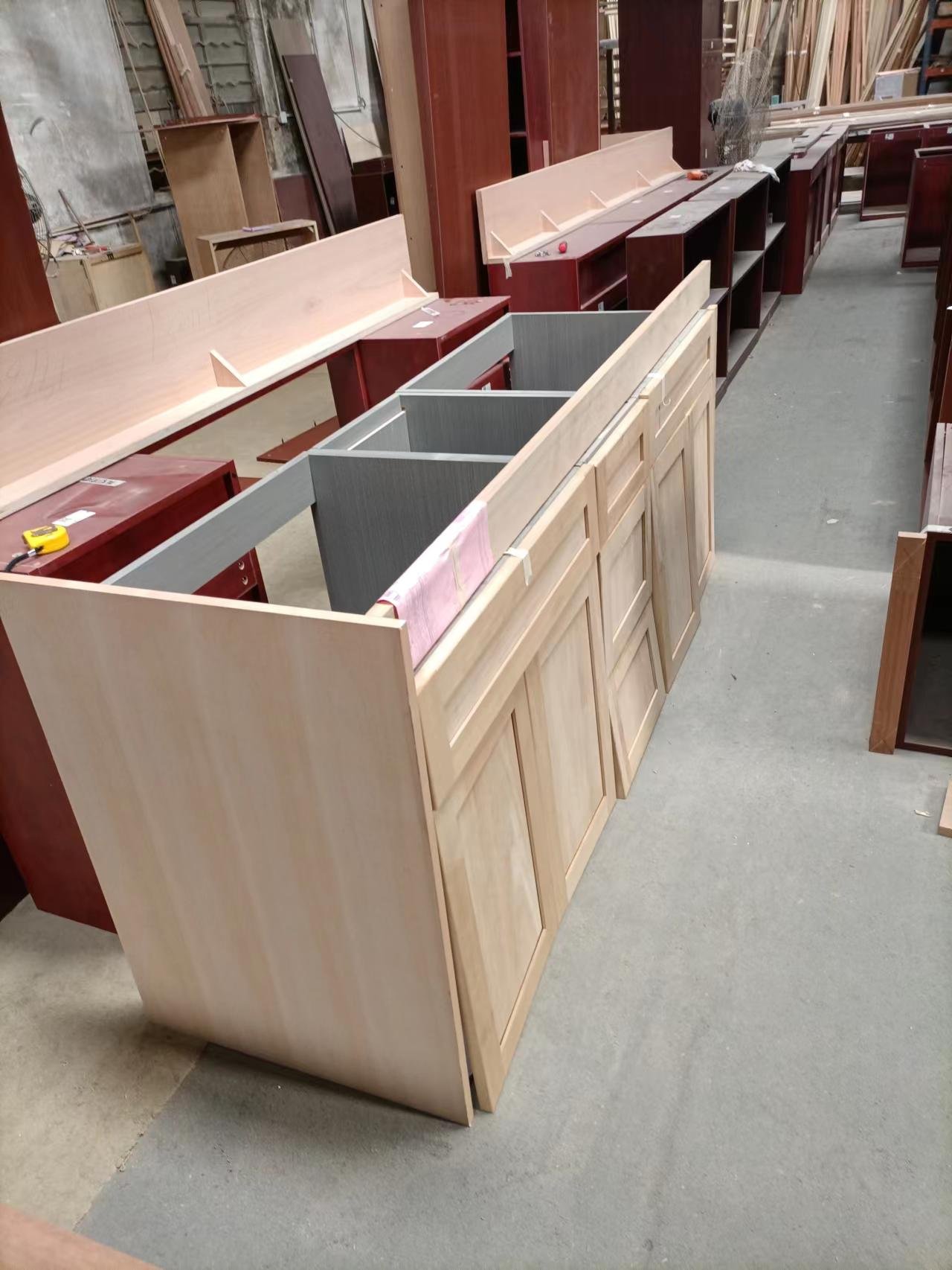Long unfinished light wood cabinet island unit with open interior compartments in workshop
