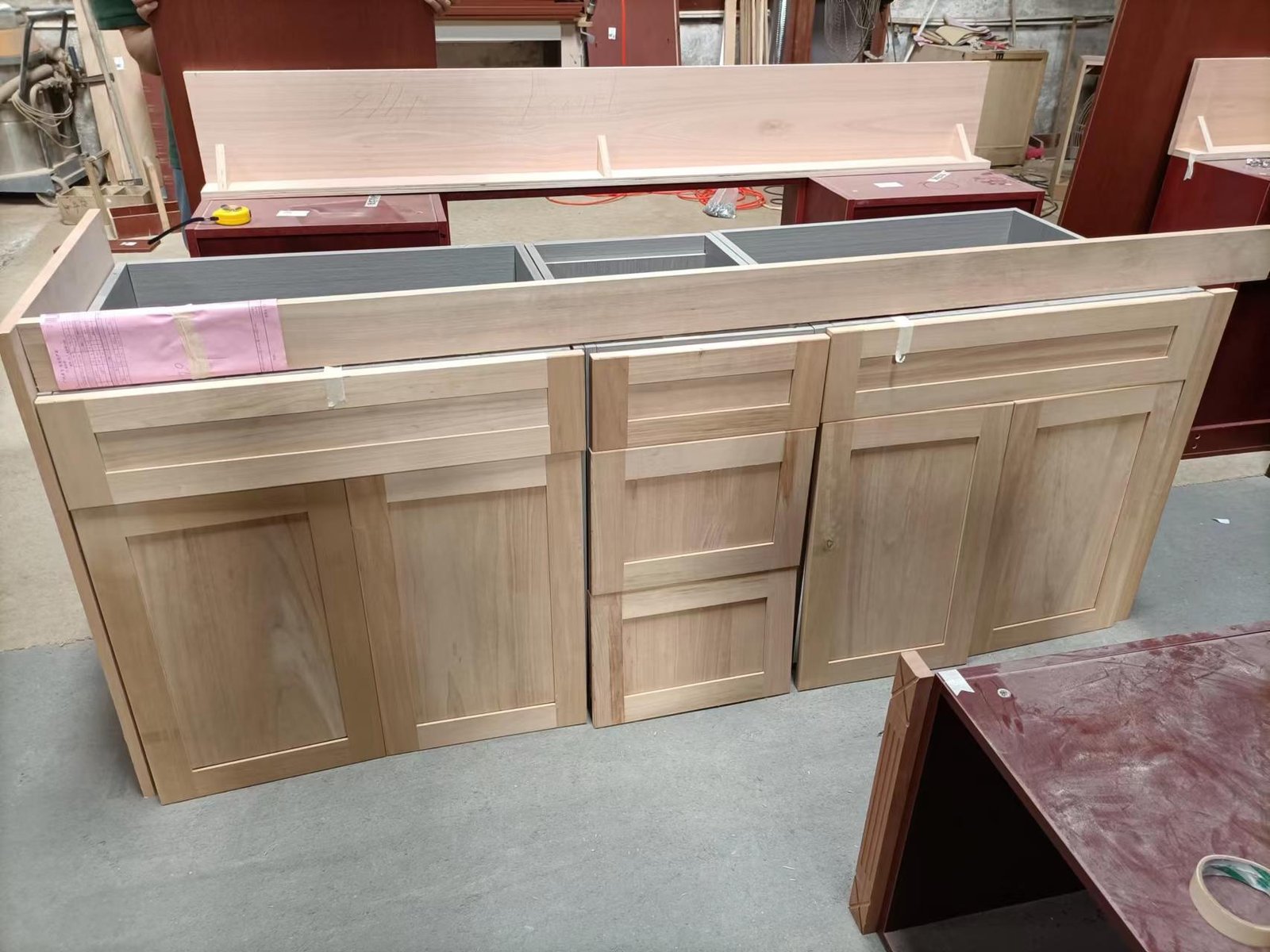 Light wood cabinet base unit with drawers and framed doors shown in factory