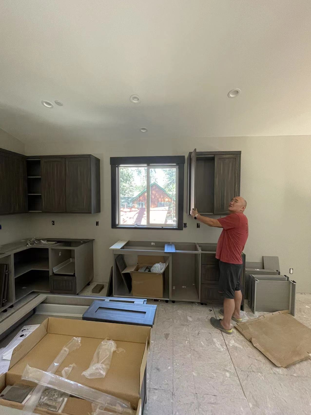 Person inspecting partially installed dark kitchen cabinets near a window on residential construction site