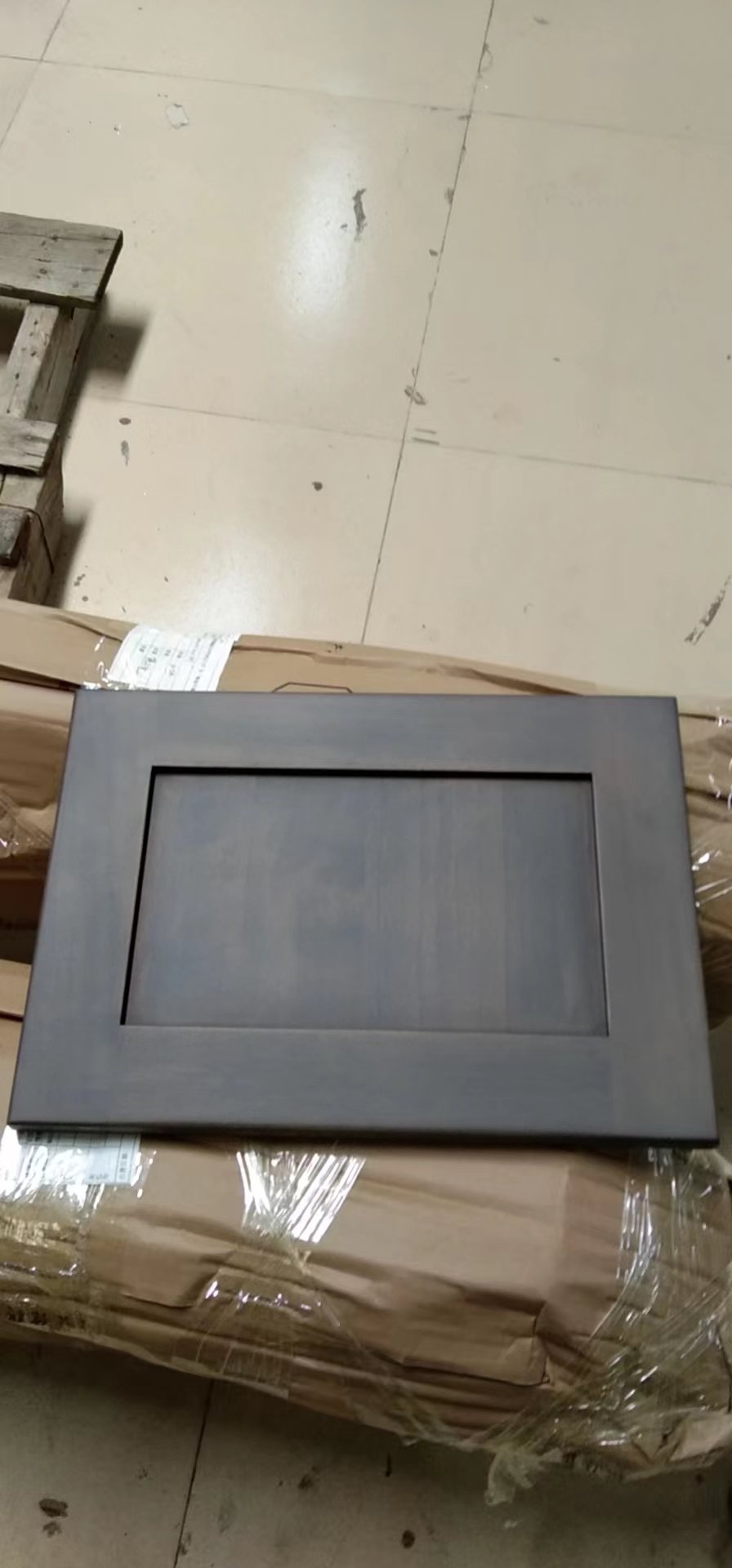 Dark gray wood cabinet door finish sample photographed over packing materials