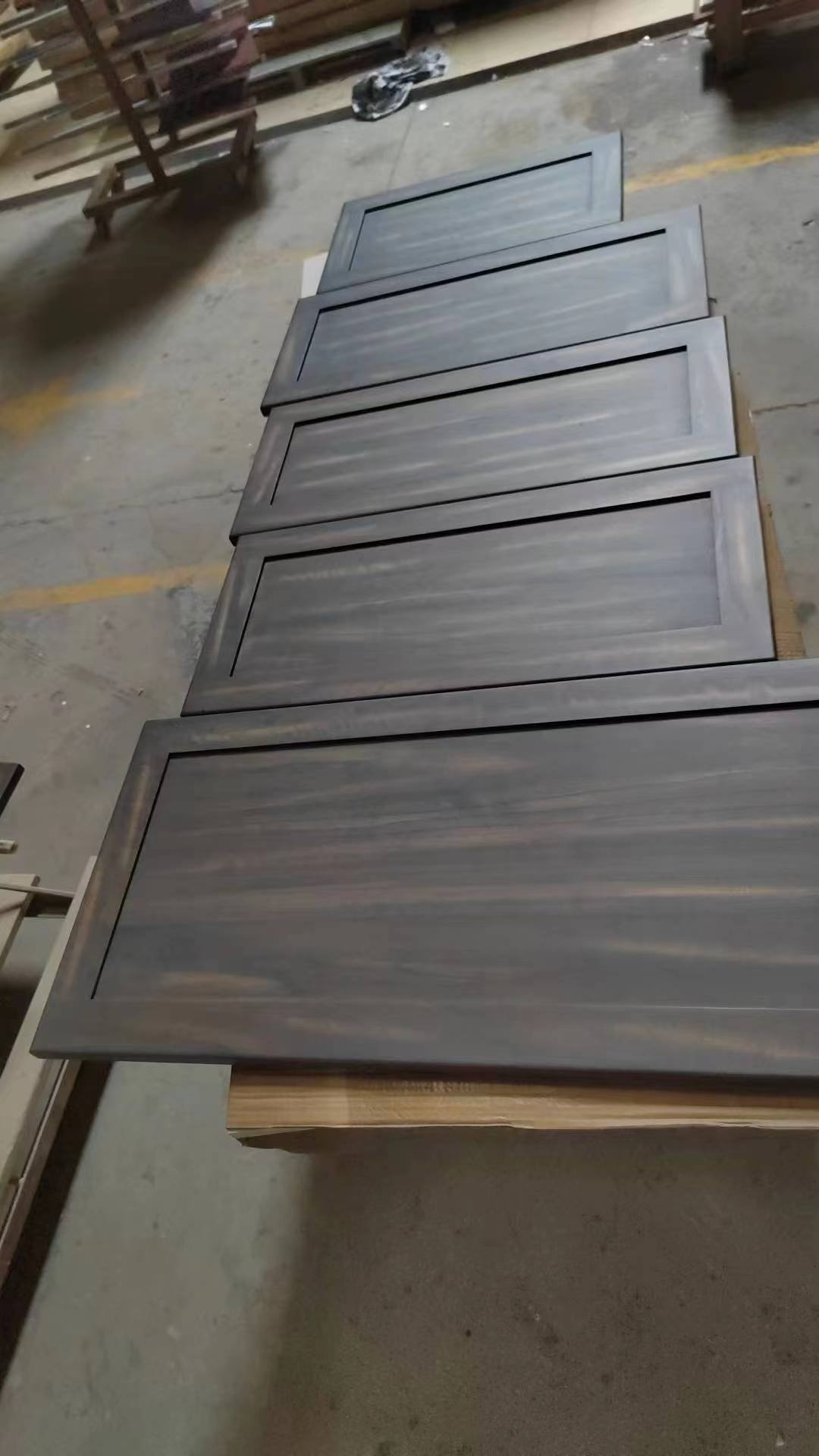 Several dark finished cabinet door panels arranged together on a workshop floor